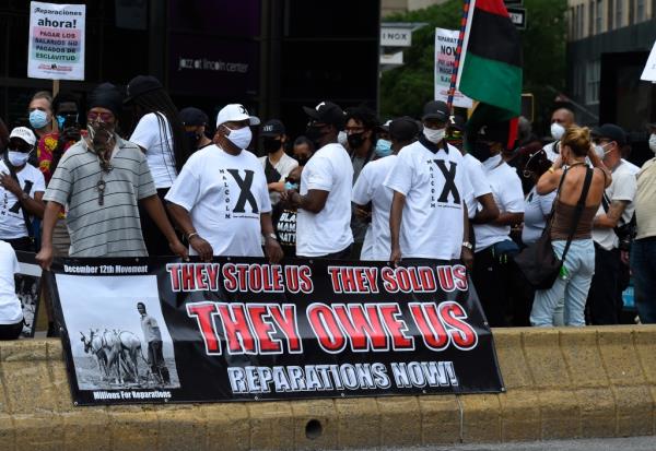 A group wearing Malcom X white T shirts protest at Columbus Circle demanding reparations for slavery of Black people in Manhattan, New York.