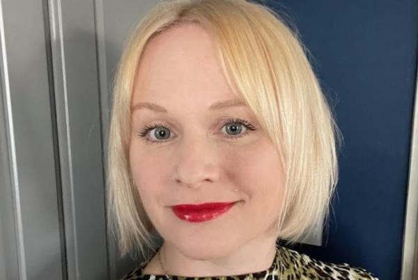 Emma Gallagher taking a selfie at home, wearing a leopard print top, white cupboards and a blue wall in the background.