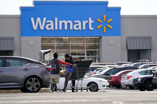 A man pushing a shopping cart in front of a Walmart store.