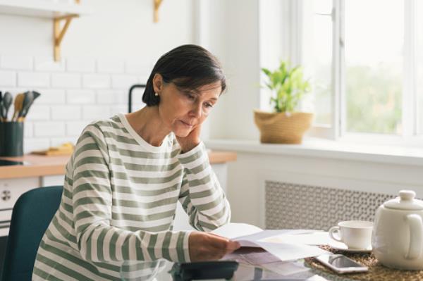 A woman in her kitchen looking at energy bills, with second Cost of Living Payment due soon