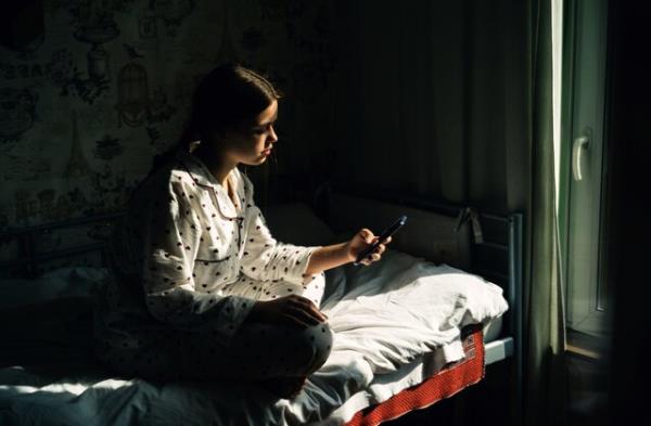 Portrait of a teenage girl with mobile phone sitting by the window in the village house. Co<em></em>ncept of depression, loneliness, problems of adolescence