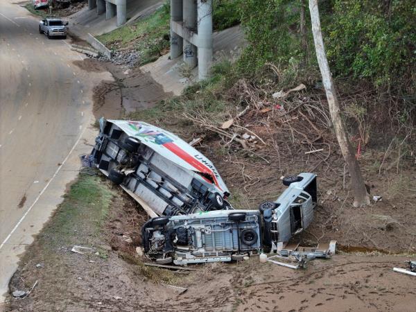 Several wrecked trucks in a ditch on the side of a highway.