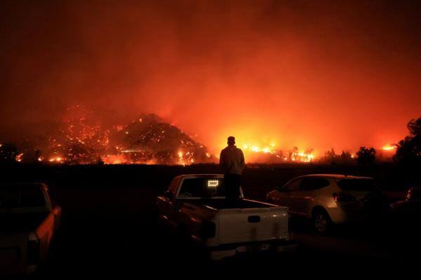 A person looks on as smoke and flames billow from the Mountain Fire in Santa Paula, California.