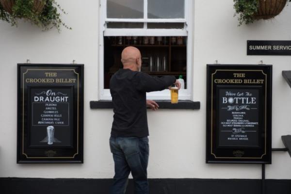 LEIGH-ON-SEA, ENGLAND - JULY 04: A customer is served a pint of beer via a window at the Crooked Billet pub on July 04, 2020 in Leigh-on-Sea, United Kingdom. The UK Government announced that Pubs, Hotels and Restaurants can open from Saturday, July 4th providing they follow guidelines on social distancing and sanitising. (Photo by John Keeble/Getty Images)