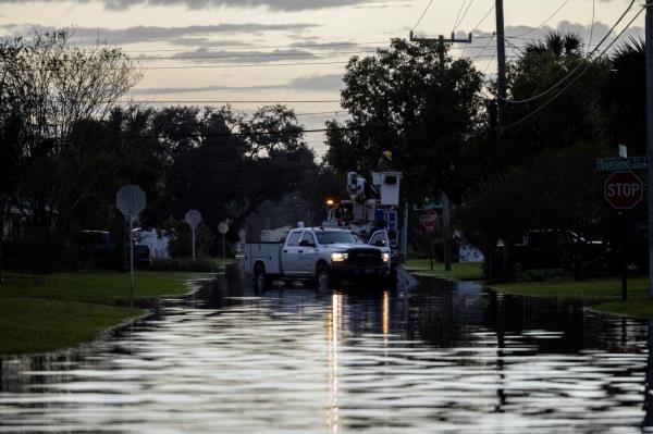 Utility workers repair a power line on a flooded street in South Daytona, Florida after Hurricane Milton landfall, with mosquitoes laying eggs in the standing water.