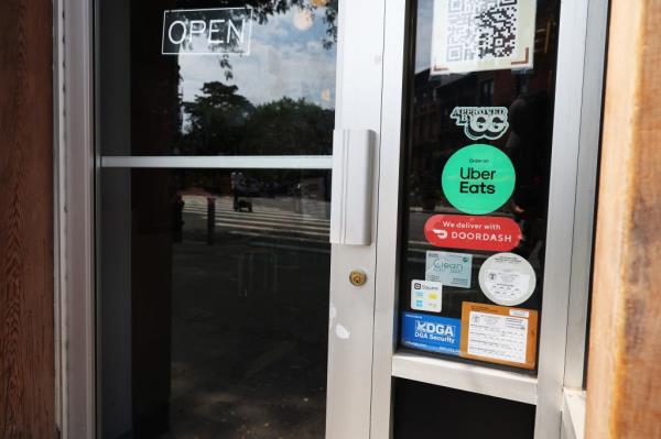 Food delivery app stickers on the window of a restaurant in Park Slope, Brooklyn, New York City, reflecting the rising prices of third-party food delivery services