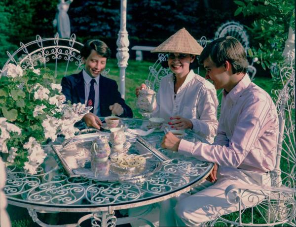 Portrait of American fashion designer & socialite Gloria Vanderbilt (1924 - 2019) (center) as she sits outdoors, drinking tea with her sons, future journalist Anderson Cooper (left) and Carter Vanderbilt Cooper (1965 - 1988), Southampton, New York, circa 1982.