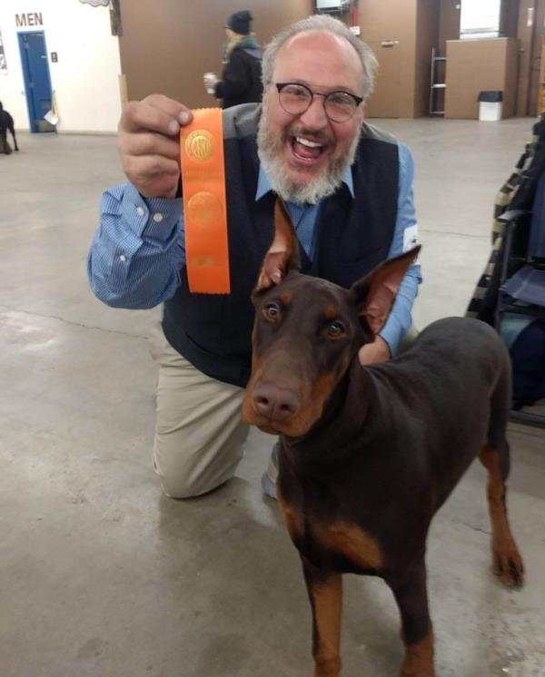 Image of a man holding a ribbon next to a Doberman. 