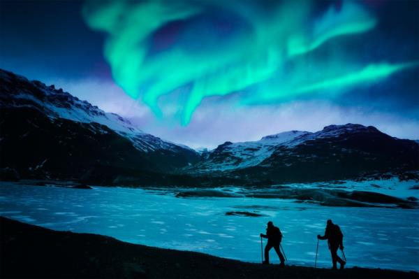 People walking on the snow with aurora borealis in the sky.