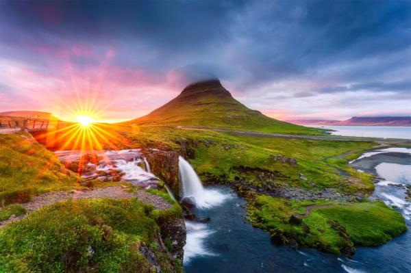 A waterfall in a grassy area with a mountain in the background.