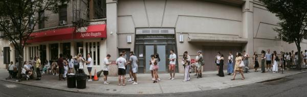 Long line of customers waiting outside Apollo Bagels in East Village, Manhattan including multiple recognizable faces amo<em></em>ngst the crowd.