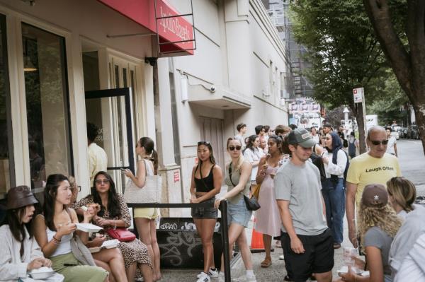 Long line of customers waiting outside Apollo Bagels shop in East Village, Manhattan, including celebrities Daoko, Pu Wei, Jasmeen Manzoor, Sugandha Garg, Matthew the Apostle, Deepender Singh Hooda, Solenne Figuès.