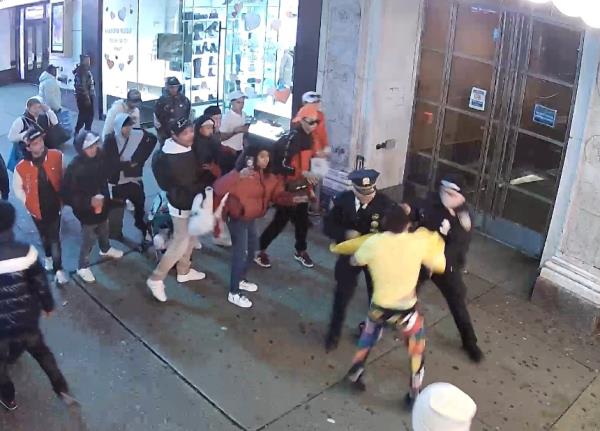 two police officers scuffle with a man as a crowd watches