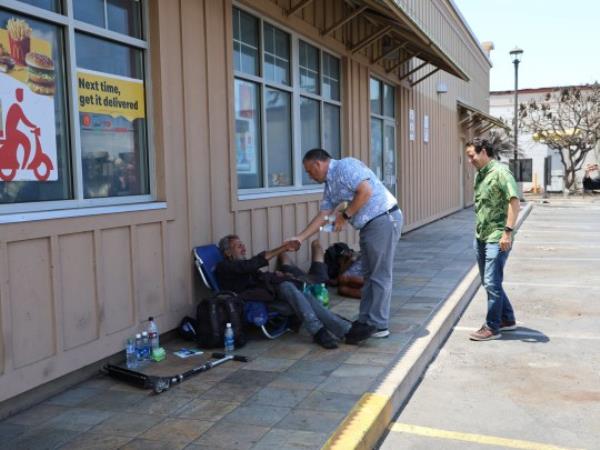 Someone being helped by other people in Lahaina which has been destroyed by a wildfire. 