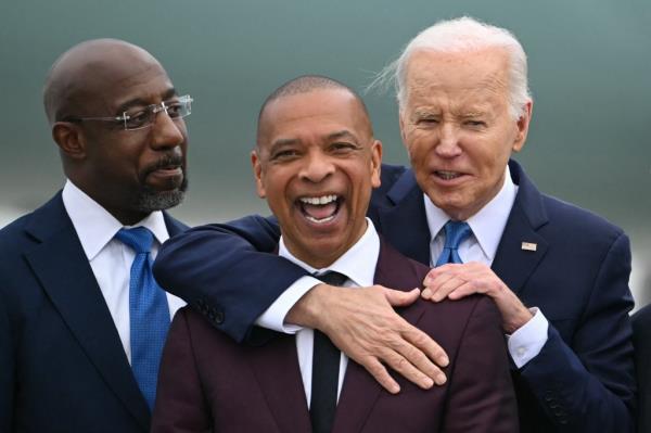 US President Joe Biden (R) embraces Marlon Kimpson (C), member of the Advisory Committee for Trade Policy and Negotiations in the Office of the US Trade Representative, as US Senator Raphael Warnock (L), Democrat of Georgia