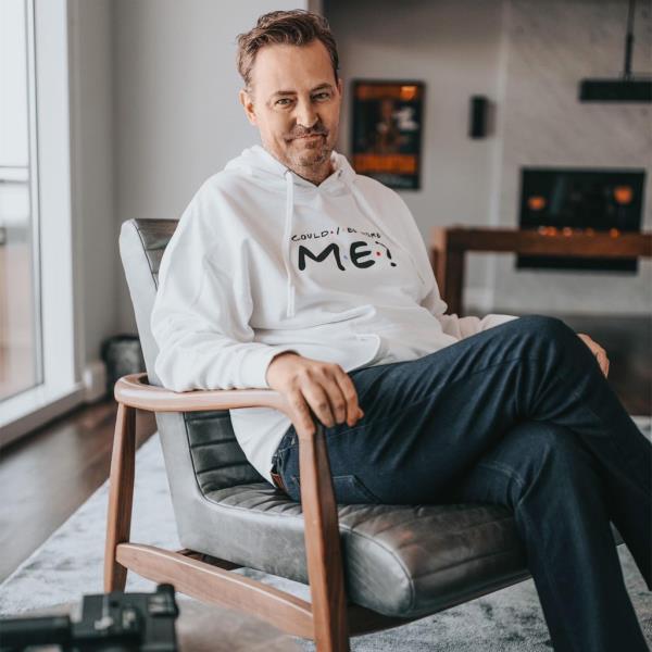 Matthew Perry smiling in a chair. 