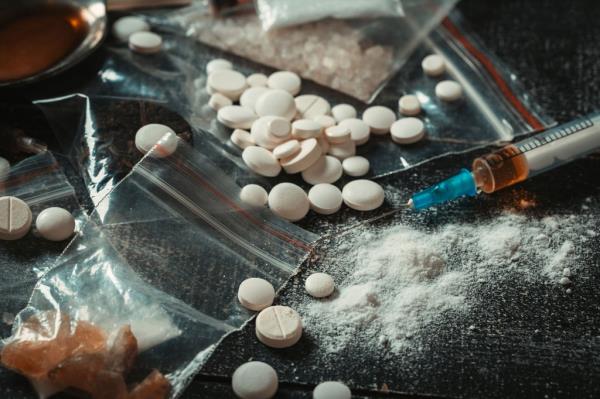 Pills, crystals, powder and a syringe on a table. 