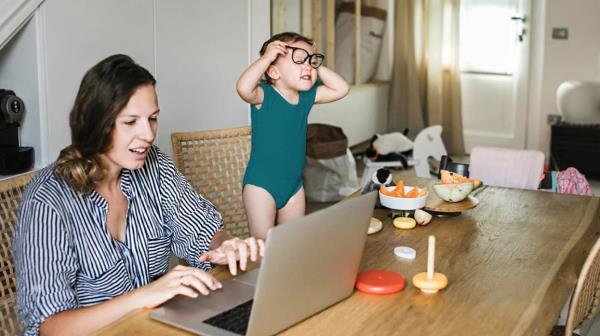 woman works on laptop while toddler plays next to her