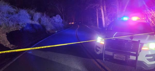 A police SUV with its lights on behind yellow crime scene tape on a rural highway.