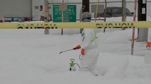 A worker in a Hazmat suit sprays a solution on knee-deep white foam 