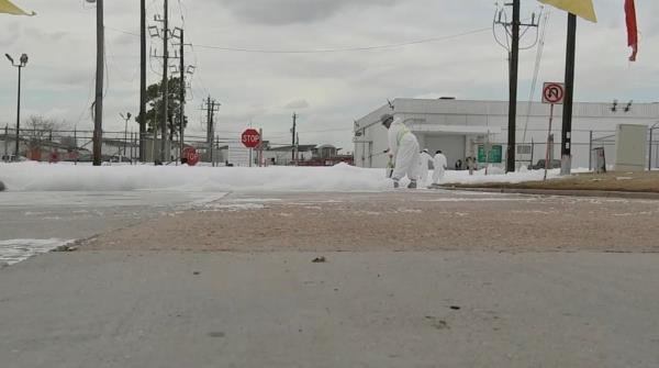 Workers in Hazmat suits spray a solution on white foam 