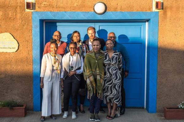 Prince Seeiso of Lesotho, Prince Harry, and others standing in front of a blue door at Sentebale's Mamohato Children's Centre in Maseru, Lesotho.