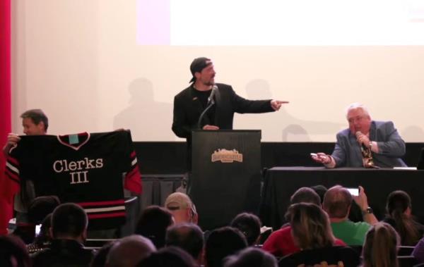 Kevin Smith speaking at a podium in front of a crowd.