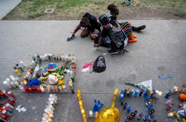 Family members co<em></em>nsole the mother of slain 16-year-old basketball star Paradisha Cooperwood, who is laying down next to a memorial for Quincy Reese Jr. in front of Crenshaw High School.