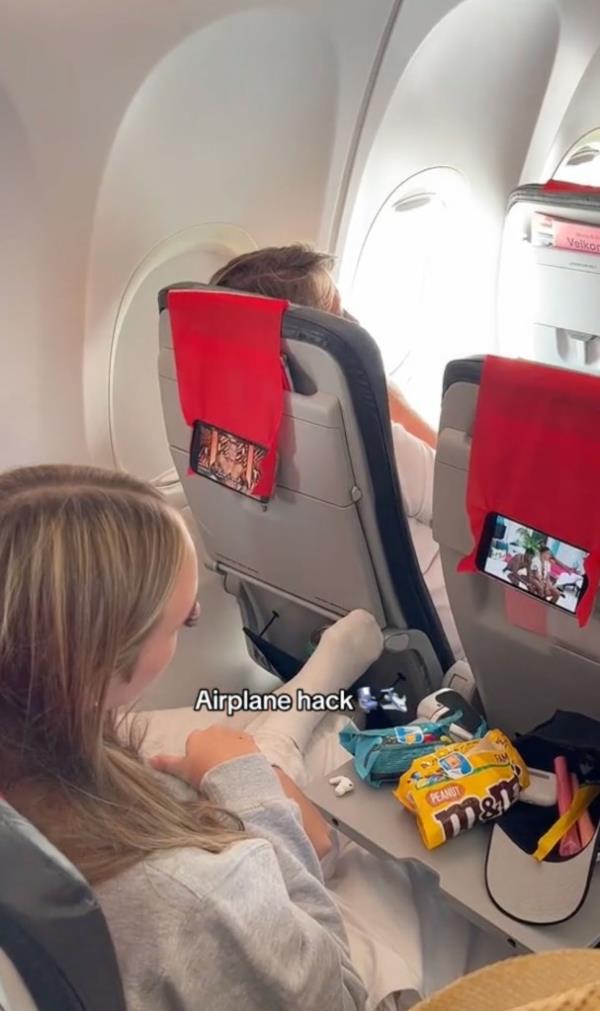 She removes her phone from its case and places it on top of the headrest cloth. She attaches her phone case from behind the fabric, so she's able to watch her phone hands-free with someone else's headrest cover.