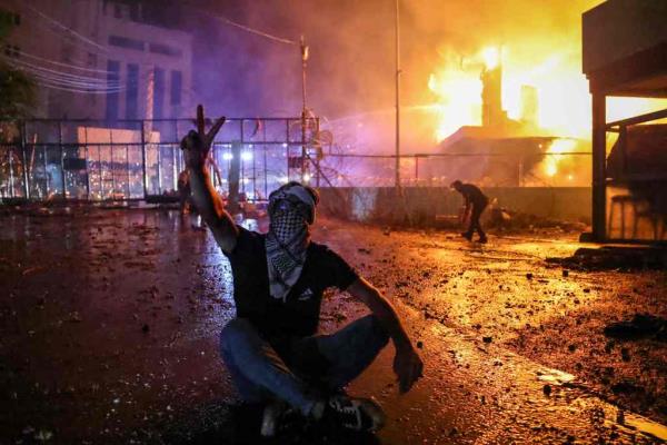 A Lebanese protester flashes the V for victory sign as a fire rages behind the security gate of the US embassy after clashes with security forces during a demo<em></em>nstration in solidarity with the people of Gaza in Awkar, East of Beirut, on Oct. 17, 2023. 