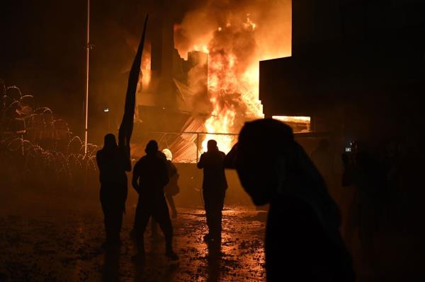 People stand in front of a fire that erupted outside the security gate, during clashes between protesters and security forces outside the US embassy in Beirut, Lebanon, on Oct. 18, 2023. 