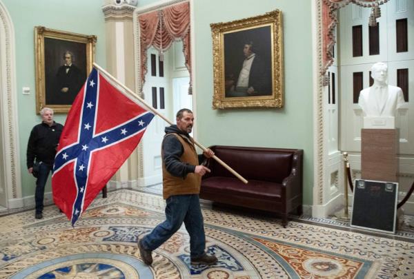 A supporter of US President Do<em></em>nald Trump carries a  Co<em></em>nfederate flag as he protests in the US Capitol Rotunda on January 6, 2021, in Washington, DC.