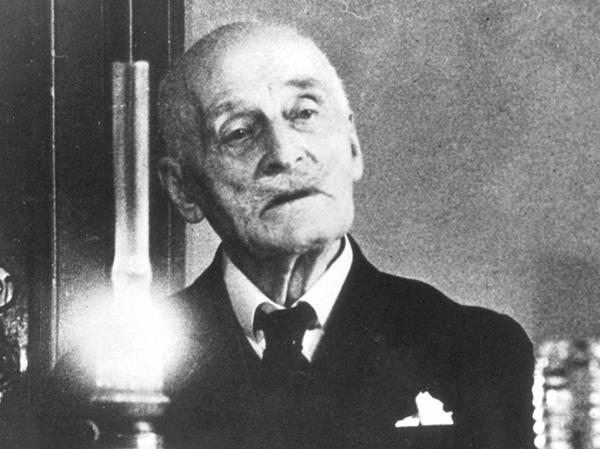 An old man sitting by a table. A kerosin lamp lights up the room. Black and white photo