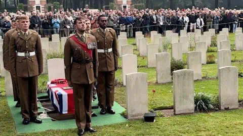 A crowd of people watch soldiers from the Royal Yorkshire Regiment stand to attention by Pte Moon's coffin in the war graves cemetery in Oosterbeek