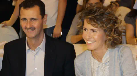 Getty Images A smiling Bashar al-Assad in an black suit with no tie, sits next to a smiling Asma al-Assad in a cardigan 